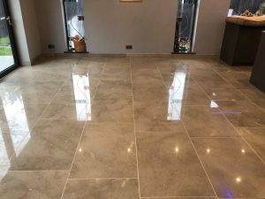 Reflective limestone floor restoration by Hardfloor Restoration Ltd with visible spotlights and bi-fold door reflections, indicating high-quality polishing services.