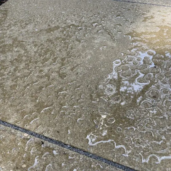 this concrete paver patio was sealed with HR total Finish Matt and the image shows the beading effect from the sealer and protection for the patio from dirt and grime. https://hardfloorrestoration.co.uk/product/hr-total-finish-matt/
