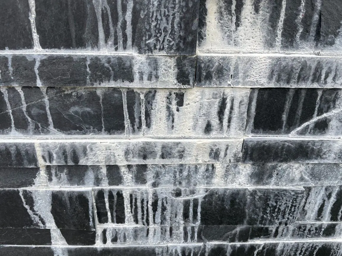 Slate wall with visible efflorescence showing white powdery stains on black slate bricks. HR Efflorescence Remover