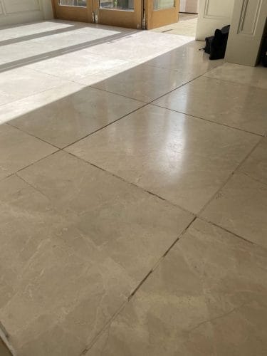 Marble floor that is in need of restoration and repair, there is missing grout in the grout lines and cracks and holes in the marble tiles, the marble floor is dull and lost its polish, this image is just before Hardfloor Restoration's marble polishing service.